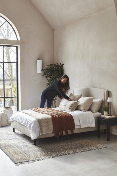 Changing bedding on a cream upholstered bed with neutral cushions, highlighting how often to change bed sheets for freshness and comfort.