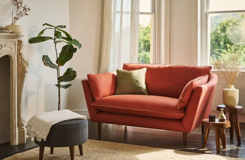 Burnt orange sofa in a soft light sitting room with a house plant and footstool